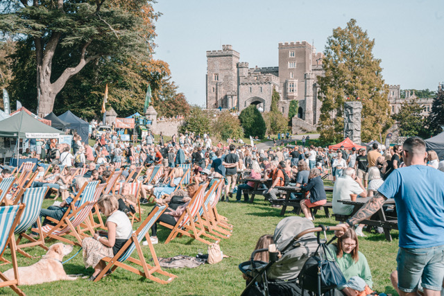 deck chairs and people sitting in the grounds of powderham castle with stalls in the background